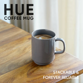 Gray coffee mug with coffee on a wooden surface, featuring the brand 'HUE'.