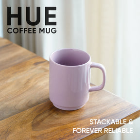 Purple coffee mug on a wooden surface with 'HUE' branding and text about stackability and reliability.