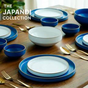 Table setting with blue and white dishes and gold cutlery on a wooden surface, featuring 'The Japandi Collection' text.