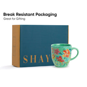 Teal mug with floral design and 'SHAY' branding in front of a blue box labeled 'SHAY'.