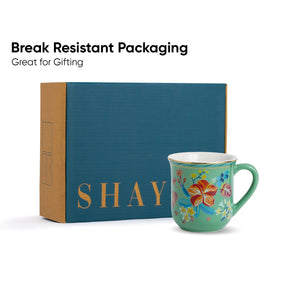 Decorative mug with floral design in front of a blue box labeled 'SHAY'.