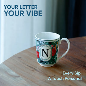 Colorful mug with a letter 'N' on a wooden surface, text 'Your Letter Your Vibe' and 'Every Sip A Touch Personal' above.
