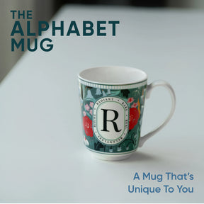 Mug with floral design and letter 'R' on a white surface, text 'The Alphabet Mug' and 'A Mug That's Unique To You' displayed.