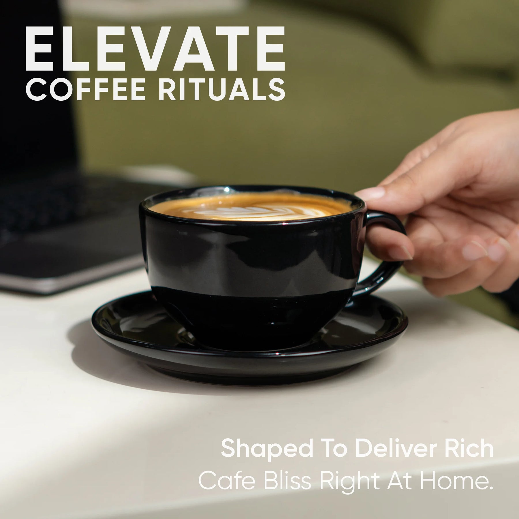 Hand holding a black coffee cup with saucer on a table, laptop in the background, text 'Elevate Coffee Rituals'.