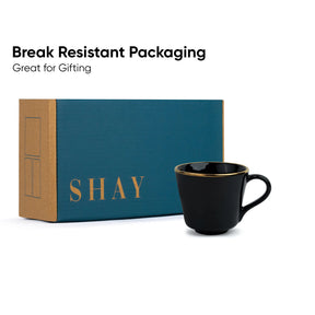 Black mug with gold rim in front of a teal and brown box labeled 'SHAY'. Text 'Break Resistant Packaging Great for Gifting' above.
