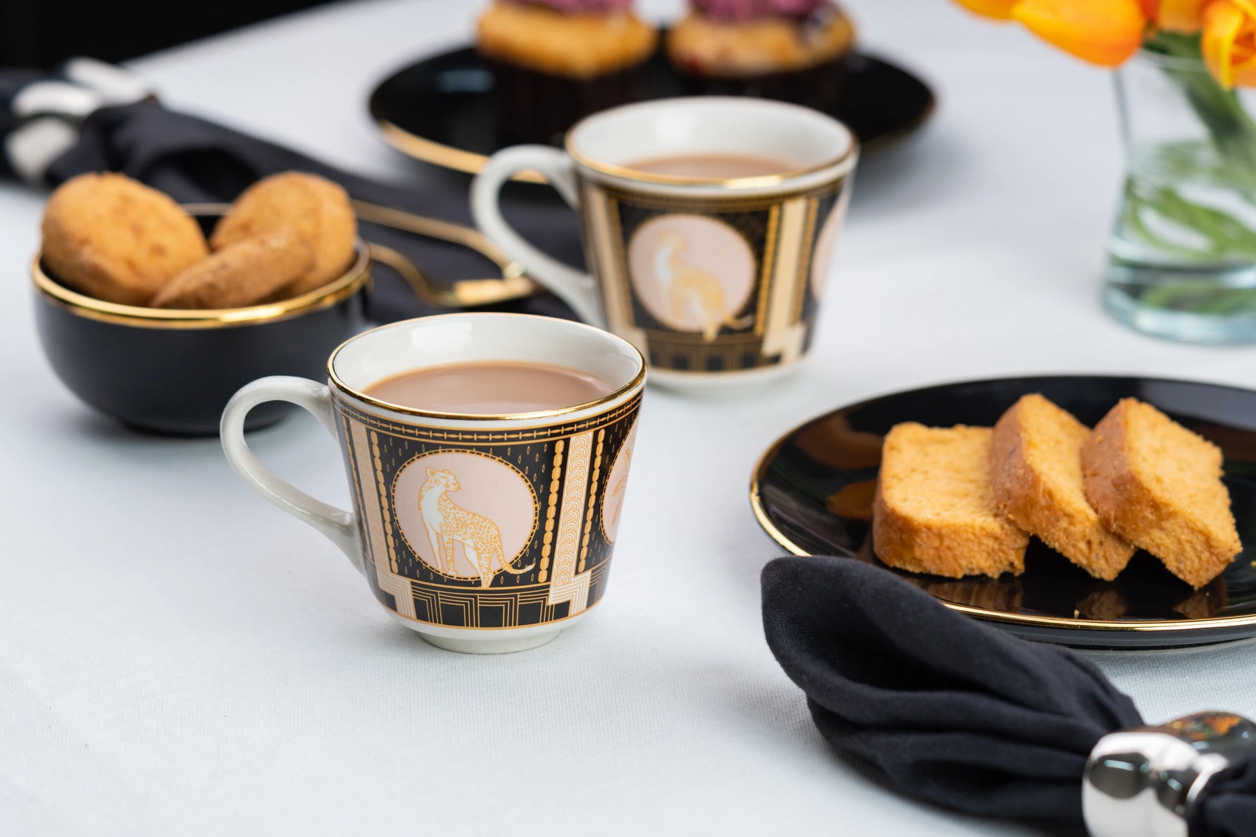 Two coffee cups with decorative patterns on a table with pastries.