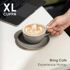 Cup of coffee with latte art on a saucer, held by a hand, with 'XL Cuppa' branding.
