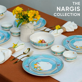 Dining table set with 'The Nargis Collection' ceramic plates, bowls, and cutlery on a brown tablecloth.
