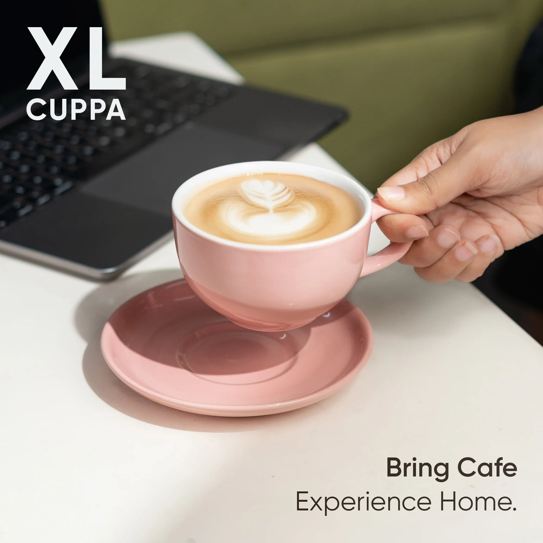 Person holding a pink coffee cup with a laptop on a desk, featuring XL Cuppa branding.