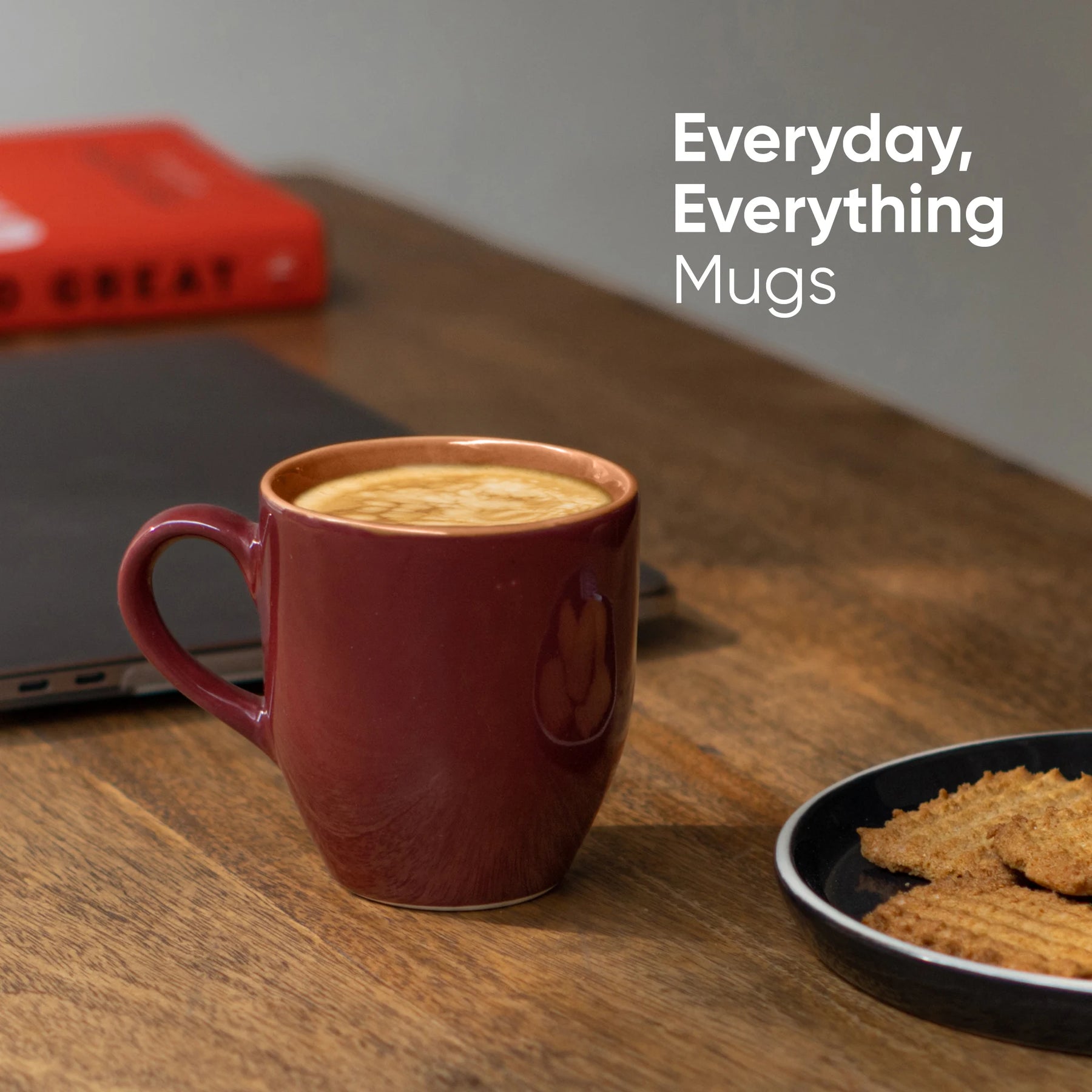Red mug with coffee on a wooden table next to a laptop and cookies, with text 'Everyday, Everything Mugs'.