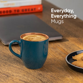 Blue mug with coffee on a wooden table with 'Everyday, Everything Mugs' text.
