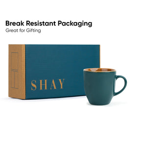 Teal mug with 'SHAY' branding next to a box, with text about break-resistant packaging.